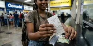 Mulher sorrindo com ticket e documento no balcão de atendimento, fila ao fundo